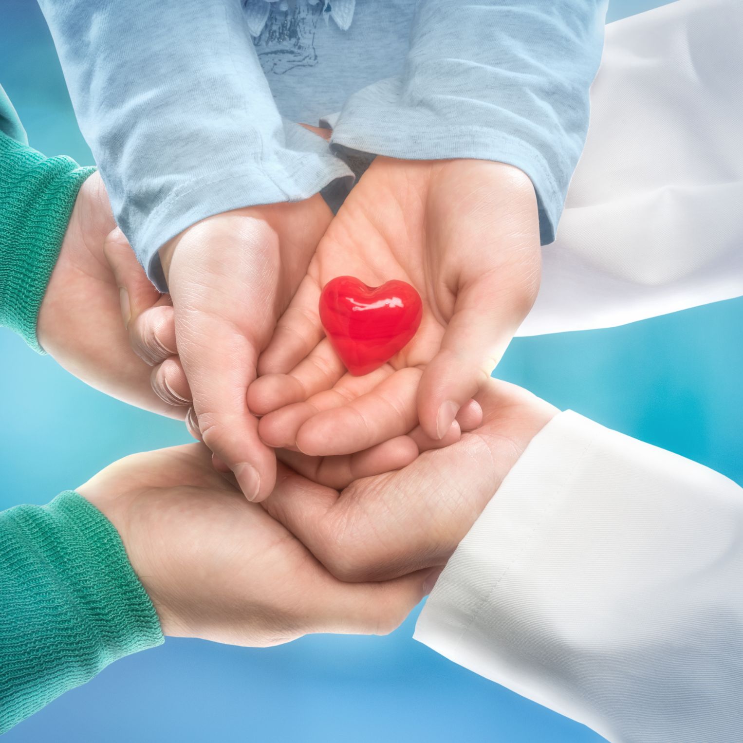 Symbolic image: Six open hands are placed on top of each other, with a red plastic or glass heart in the top one.