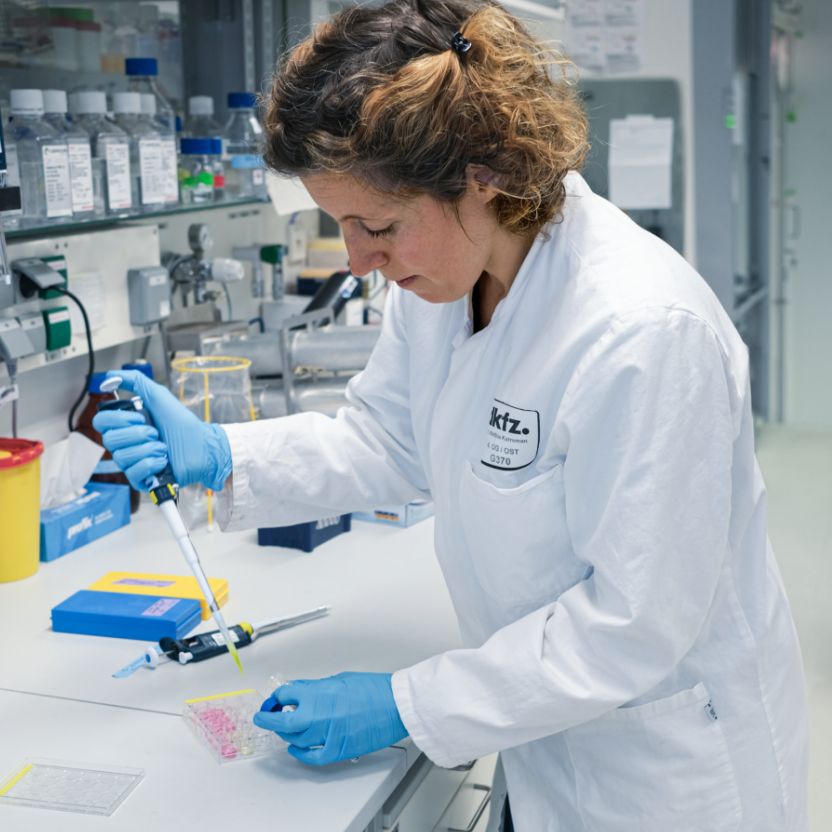 A person wearing a white coat and gloves is working with a pipette.