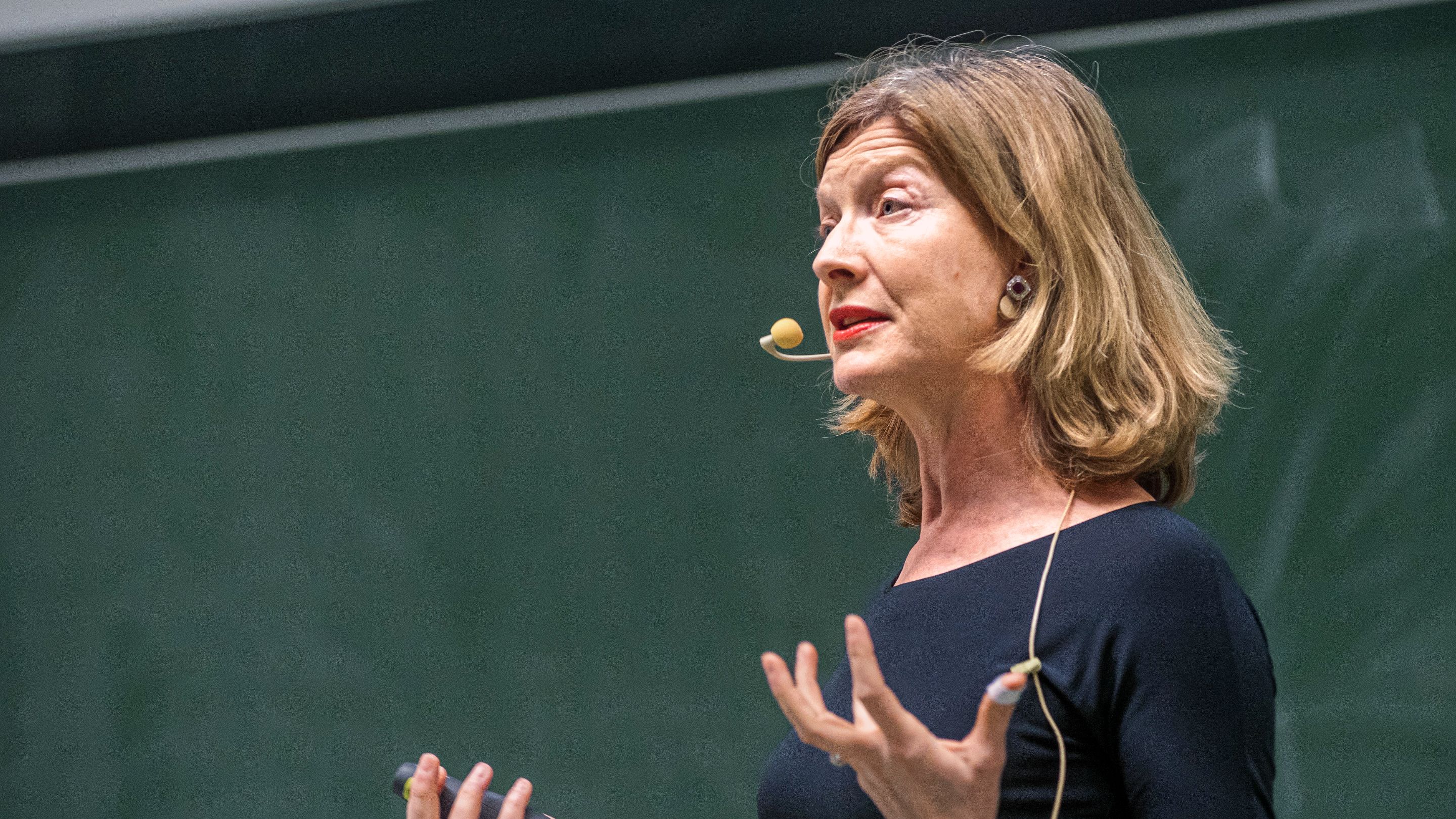 Prof. Dr. Hannah Monyer speaks into a microphone in front of a blackboard &ndash; a lecture situation.