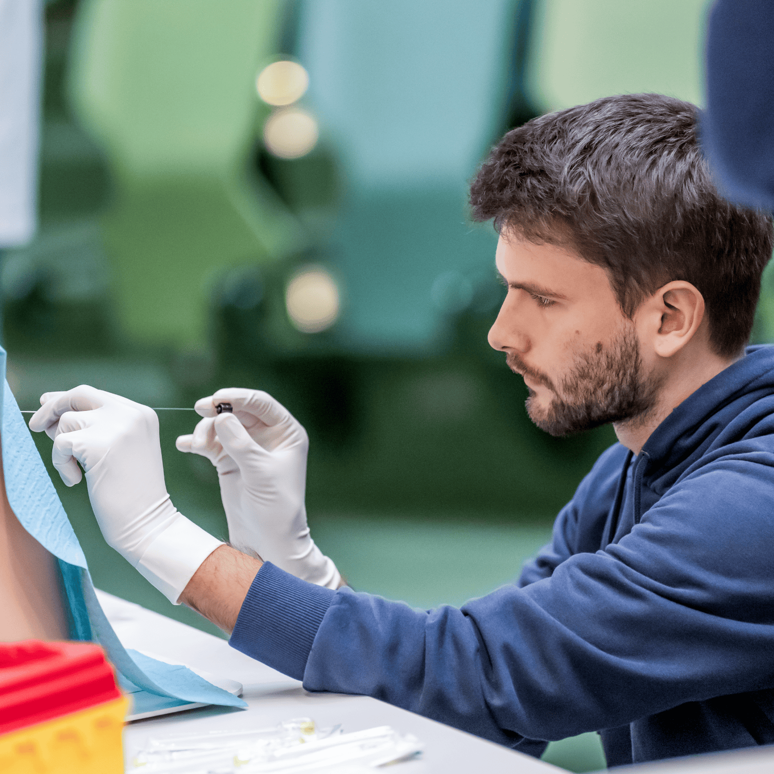 Practical exercise in the skills lab: a young man wearing white gloves holds a long needle to a model of a human back.